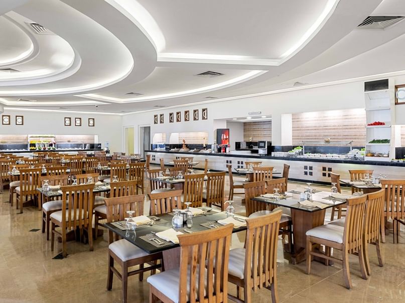 A large, empty restaurant with wooden tables and chairs, a curved ceiling, and a counter with food displays.