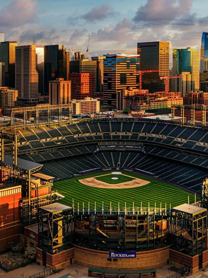 Aerial view of Coors Field Stadium by city buildings under a sunset sky near Warwick Denver