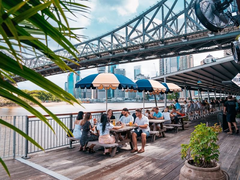 Outdoor dining by a river with a bridge at Howard Smith Wharves near Sofitel Brisbane Central