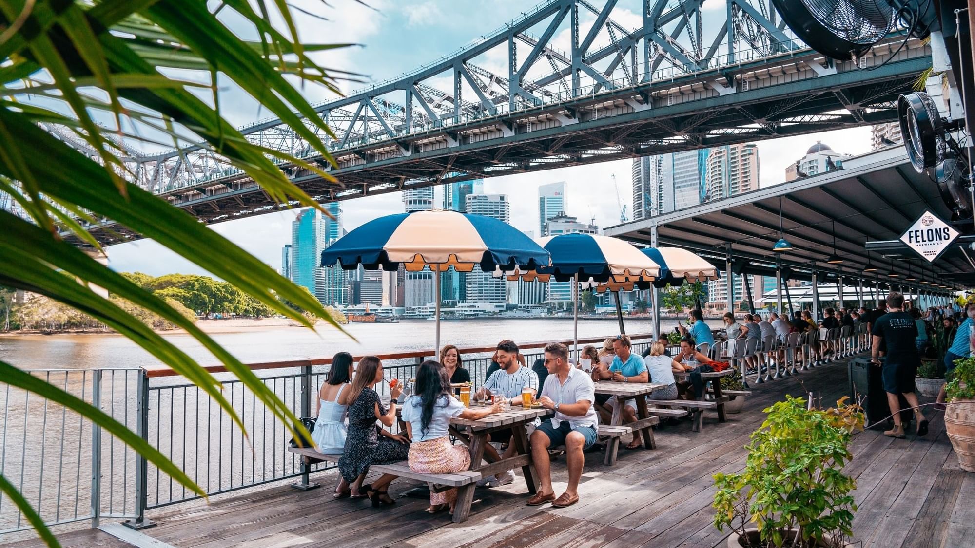 Outdoor dining by a river with a bridge at Howard Smith Wharves near Sofitel Brisbane Central