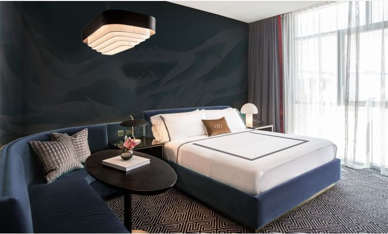 Silver king bed & dark blue sofa set in room at Dream Doha.