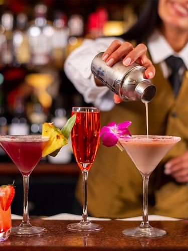 Bartender pouring drink into glass among colorful array of tropical cocktails in Randolph's Bar & Lounge at Warwick New York