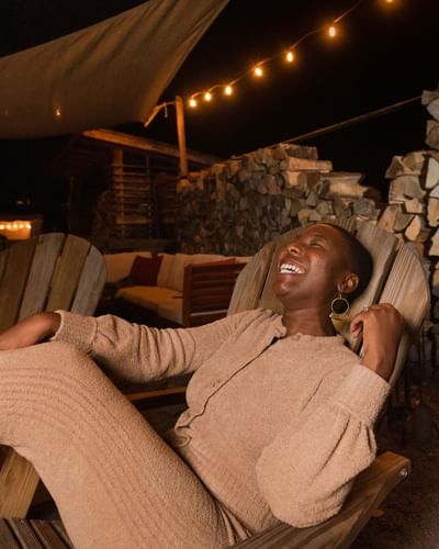 Woman laughing on a wooden Adirondack chair near stacked firewood at night at La Tourelle Hotel and Spa