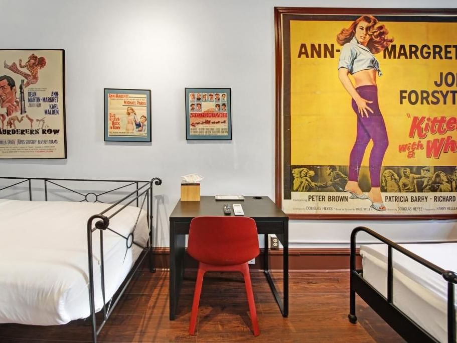 One Bedroom Suite with two beds, desk, chair, and movie posters at Chelsea Pines Inn in New York.