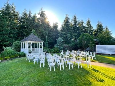 Chairs arranged in rows on a lawn with a gazebo in the background and lush greenery.