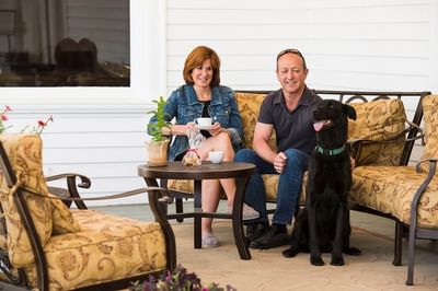 A man and woman sit on an outdoor patio at The Stanley Hotel petting their dog and enjoying a beverage