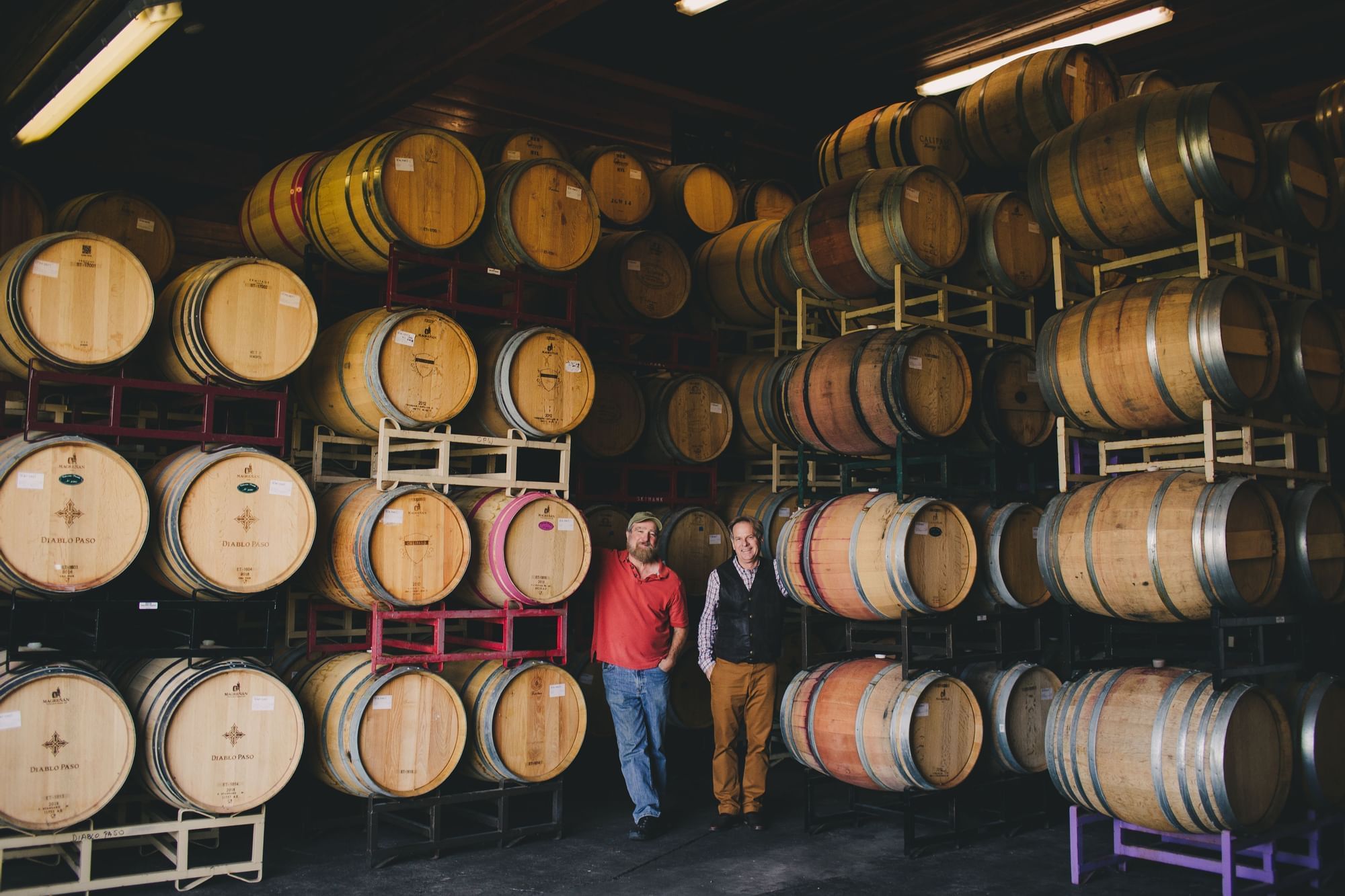 Two men standing by stacks of wine barrels