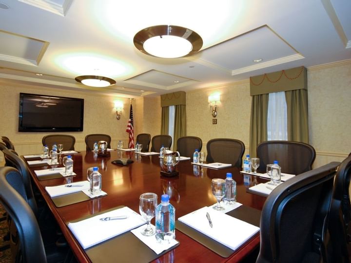 A large, well-lit meeting room with a long table, chairs, a screen, and an American flag.