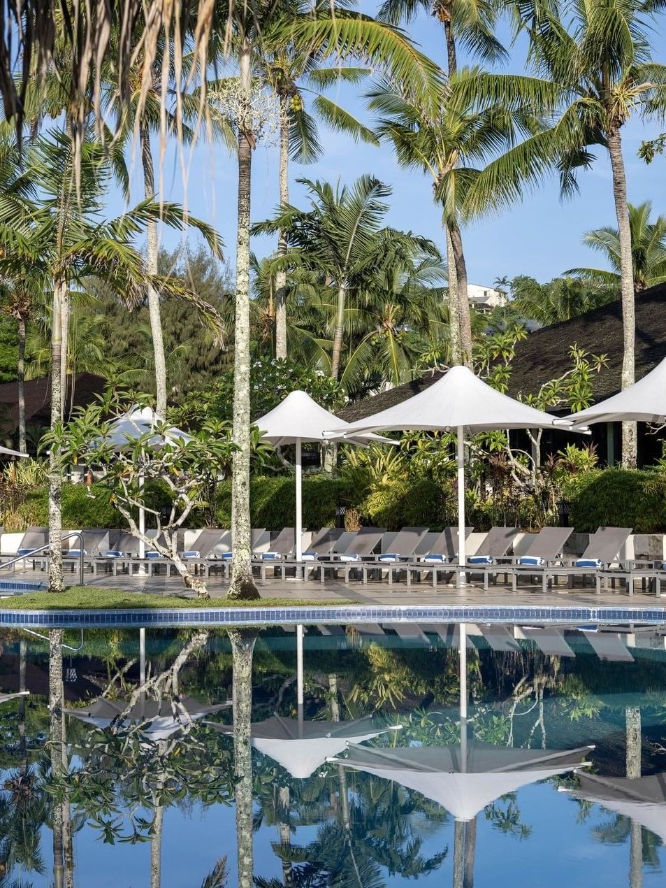 Serene pool with lounge chairs and umbrellas surrounded by lush palm trees at Warwick Le Lagon Vanuatu