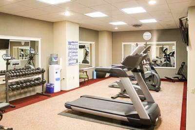 Treadmill by stationary exercise bikes under square ceiling lights in a bright fitness room at Rodd Charlottetown Hotel