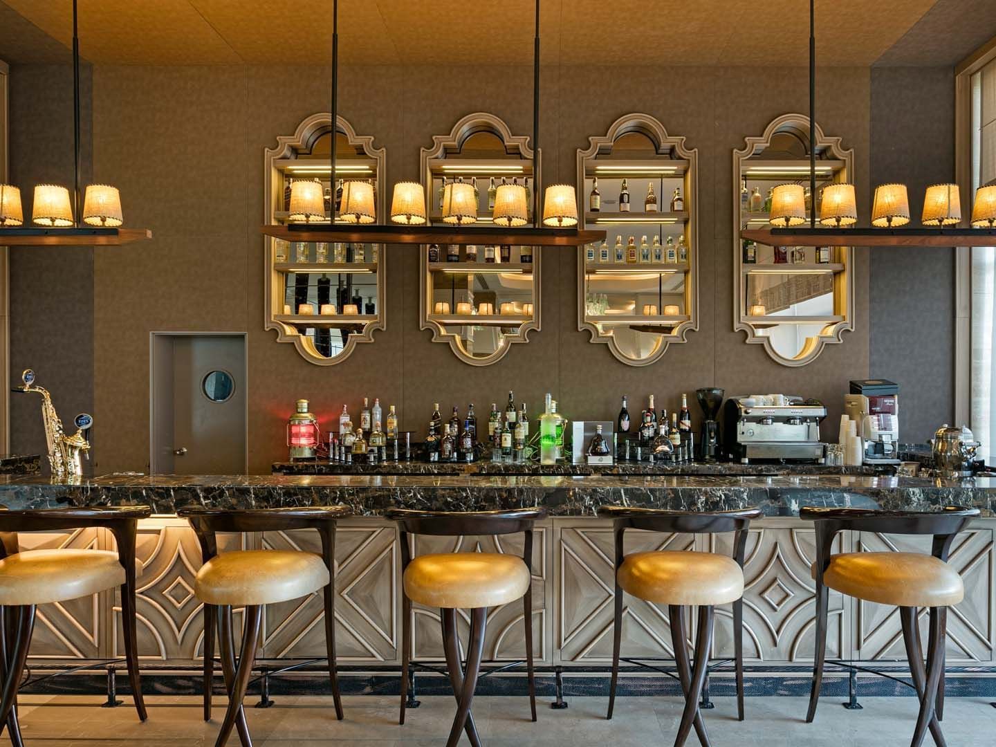 Cordelia Lobby Bar with stools, hanging lights, and shelves of liquor and glasses at Titanic Deluxe Lara