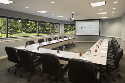 Modern conference room with U-shaped setup, chairs, projection screen, and garden views at Aramark Chauncey Conference Center