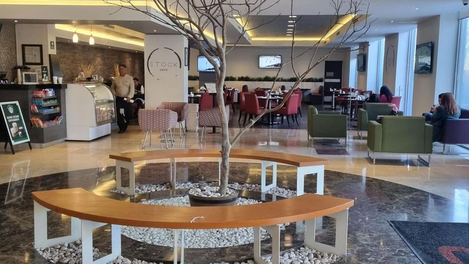 Stock Cafe featuring a central decorative tree, circular wooden bench, and marble floors at Real Inn Perinorte