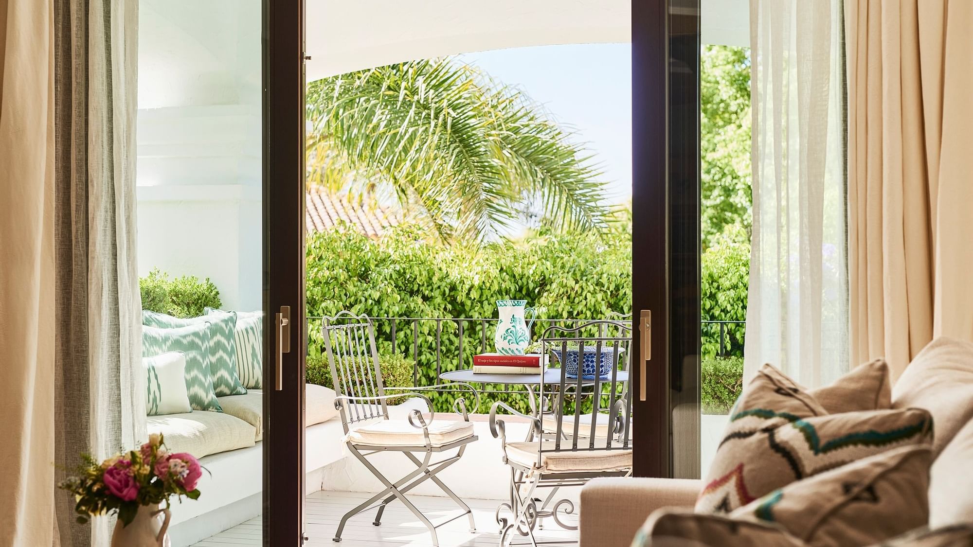 Santa Margarita Two-Bedroom Suite living space opening to a terrace with metal chairs & lush greenary at Marbella Club