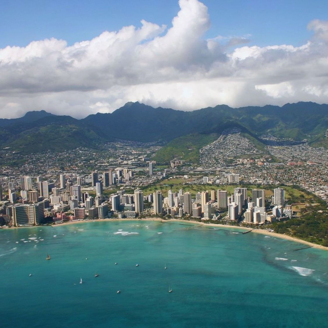 A sunny aerial view of Waikiki Beach, Oahu, showing the calm spring waters and the vibrant resort district where the 30th Honolulu Festival and Prince Kūhiō Day celebrations take place in March 2026.