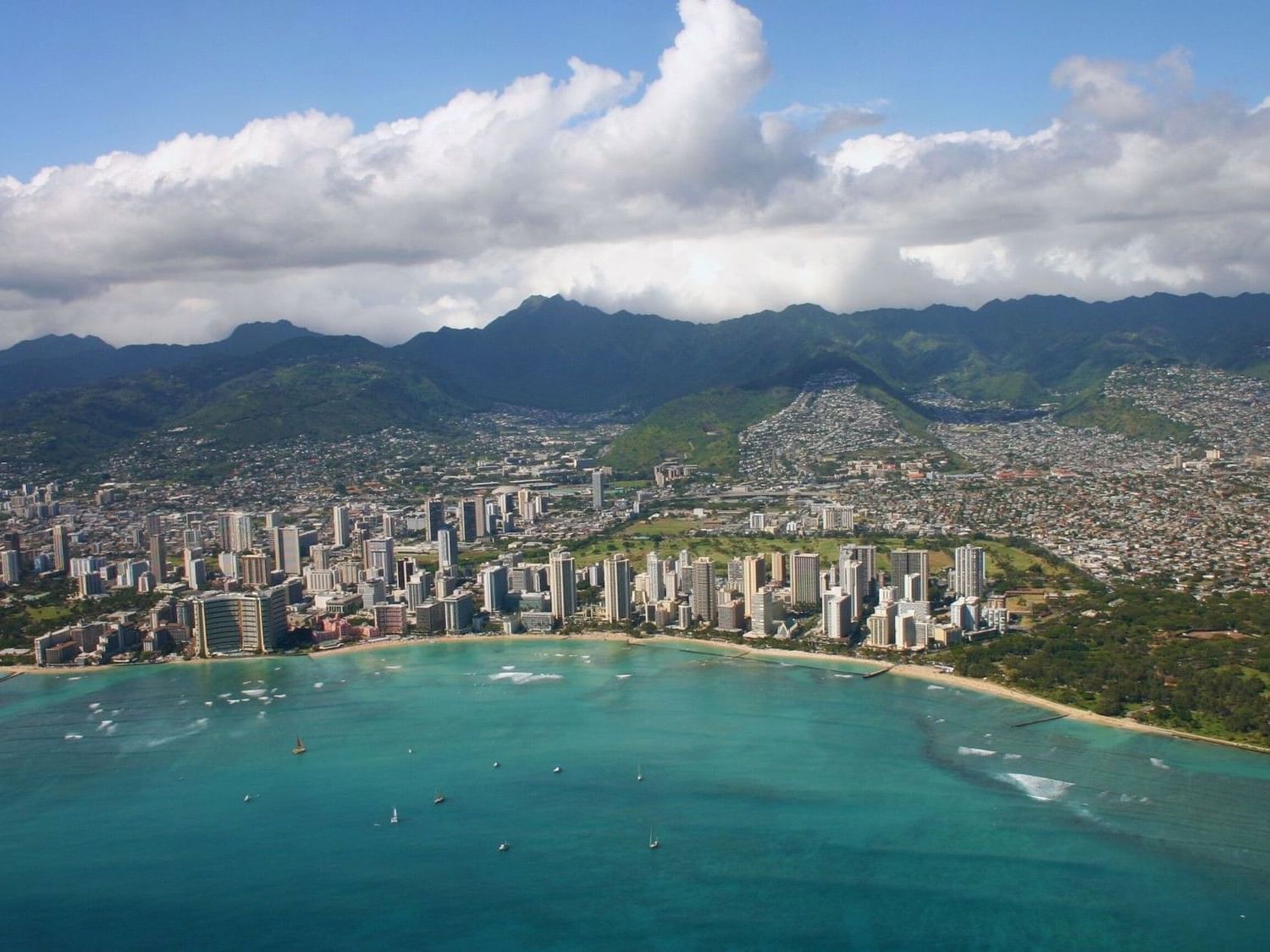 A sunny aerial view of Waikiki Beach, Oahu, showing the calm spring waters and the vibrant resort district where the 30th Honolulu Festival and Prince Kūhiō Day celebrations take place in March 2026.