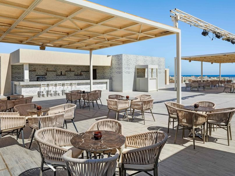 Outdoor dining area with tables and chairs under a canopy, with a view of the ocean.
