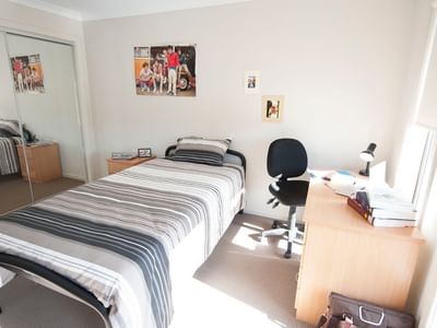 A neat single room with a bed, desk, and chair at La Trobe University Regional Housing Shepparton.
