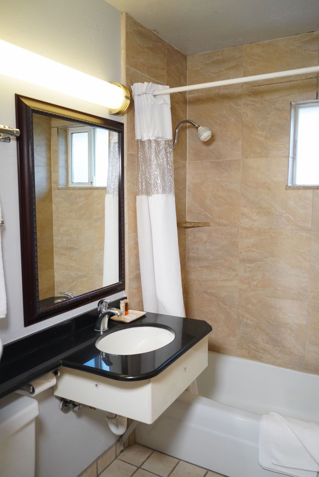 A standard bathroom with tan tile walls, a black countertop, and a tub/shower combo.