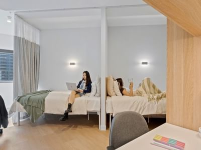 Two women in beds, one reading a book and one on a laptop, at UniLodge Brisbane City.