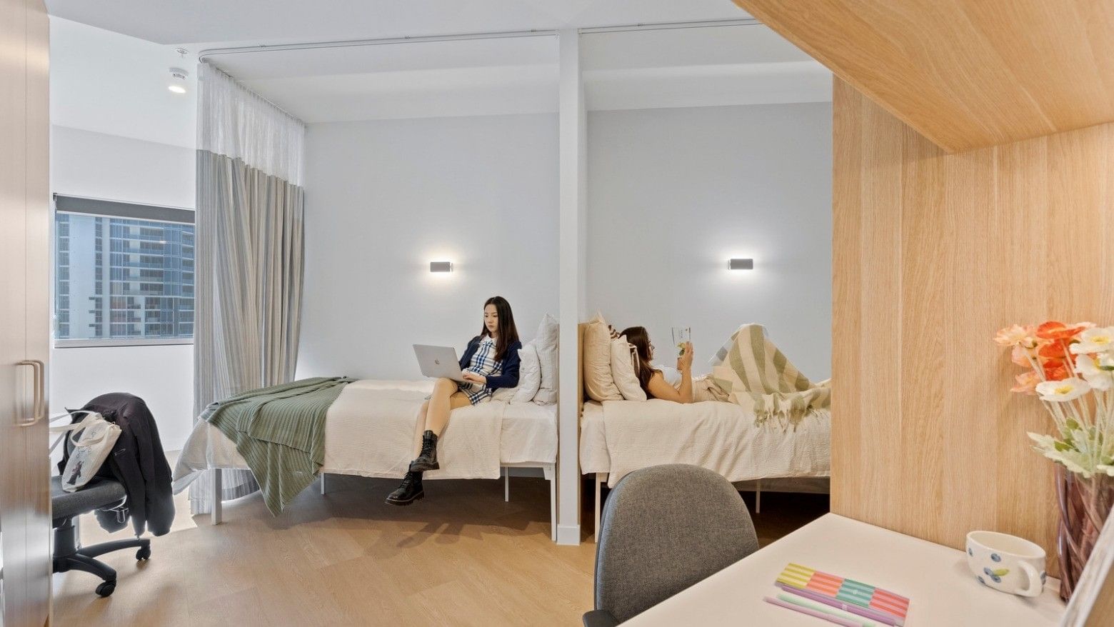 Two women in beds, one reading a book and one on a laptop, at UniLodge Brisbane City.
