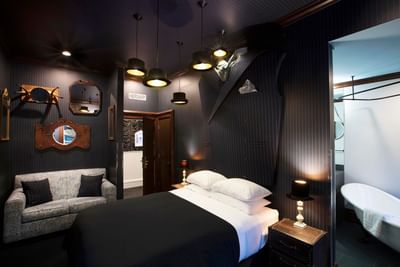 Large suit coat on the wall, bed, mirrors, and elegant lighting in The Dashing Haberdasher at The Roxbury