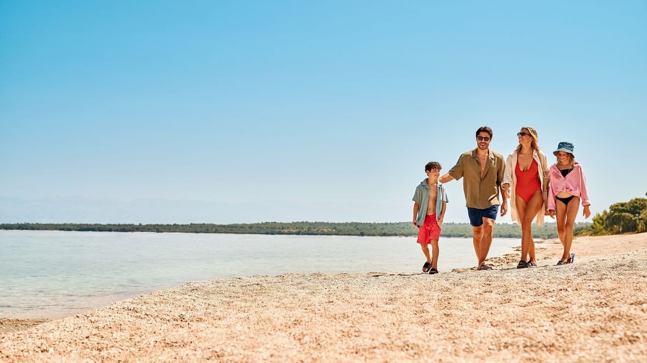 Familie mit zwei Kindern, Eltern und Großeltern spazieren am Strand entlang des Ozeans.