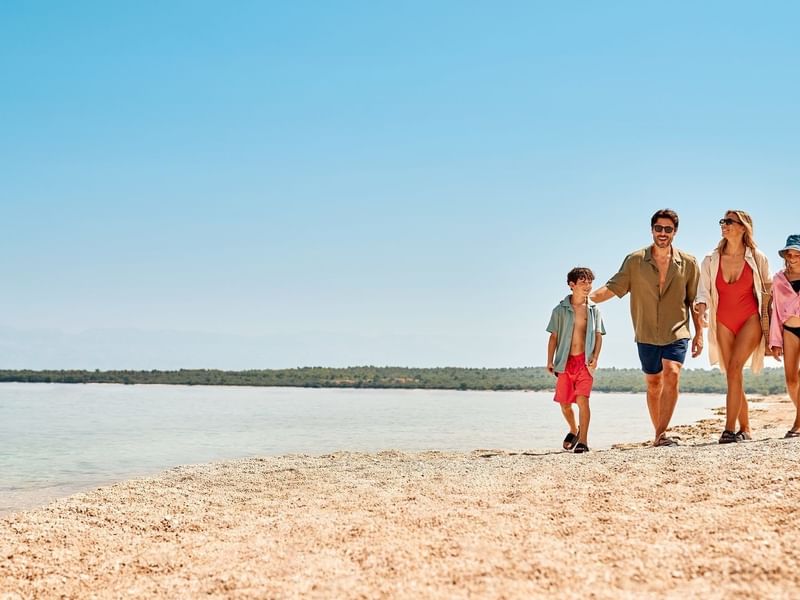 Familie mit zwei Kindern, Eltern und Großeltern spazieren am Strand entlang des Ozeans.