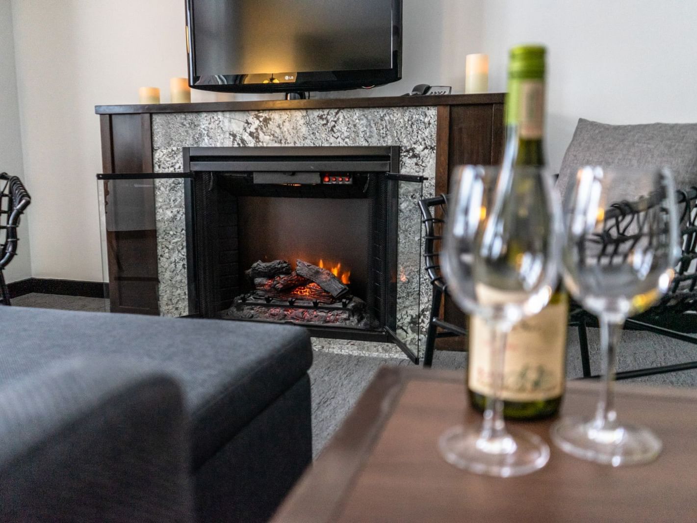 Wine bottle and glasses on table next to couch facing tv and fireplace