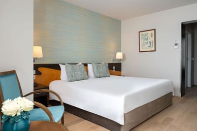 Room featuring a double bed, soft blue-green wall, wooden accents, and a cozy seating area at Ana Hotels Europa Eforie Nord