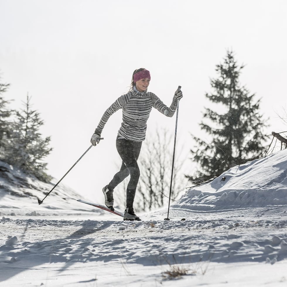 Una donna con sci e bastoncini da sci sulla neve, con alberi sullo sfondo.