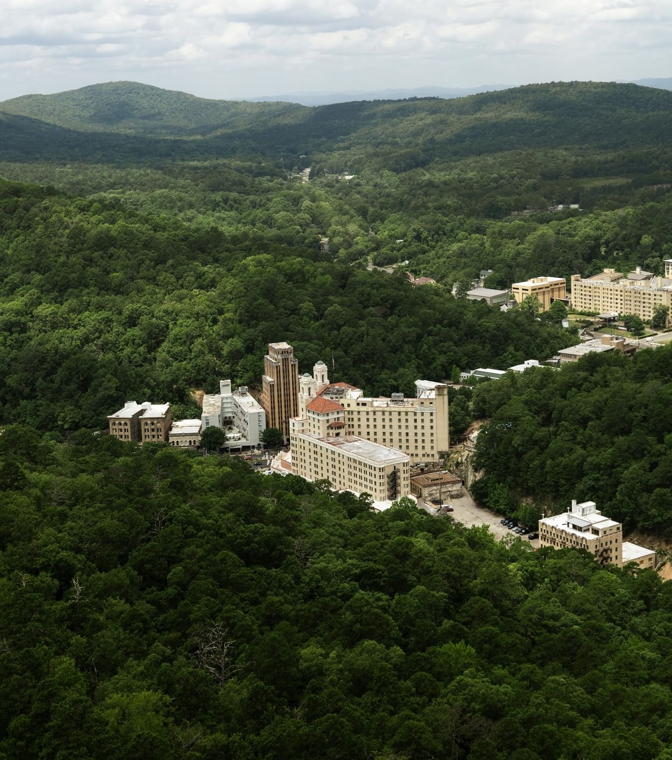 Aerial view of Arlington Resort Hotel & Spa amid lush forested hills and rolling mountains beneath a bright, cloudy sky