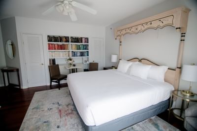 King bed with ornate wooden canopy frame and bookshelves beside a small seating area at La Tourelle Hotel and Spa
