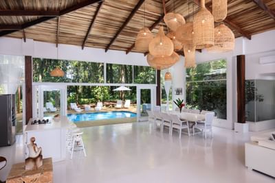 Frida Villa’s bright living space with pool view, rattan lights, modern furniture, and lush greenery outside at Le Cameleon