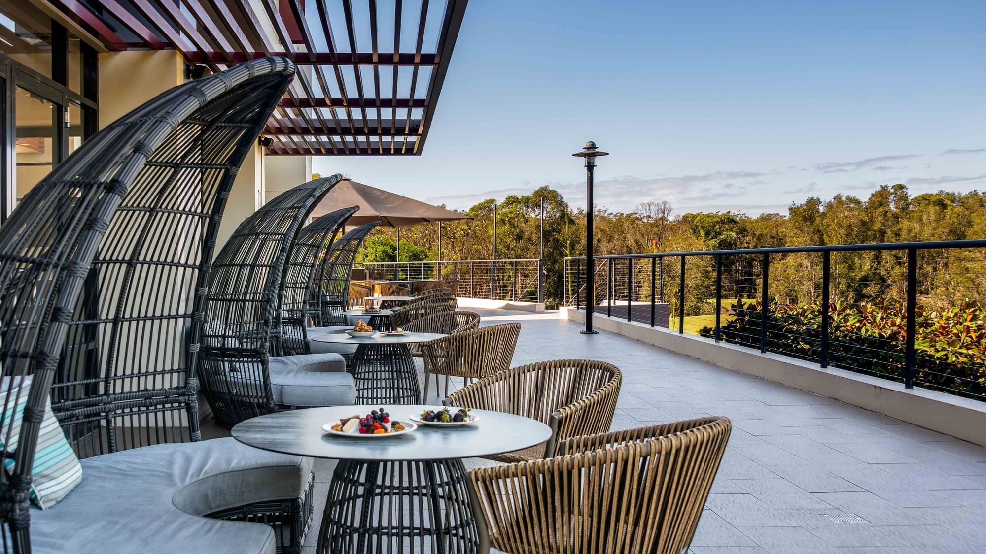 Karinyas Terrace with wicker furniture and a fruit platter overlooking greenery at Mercure Kooindah Waters