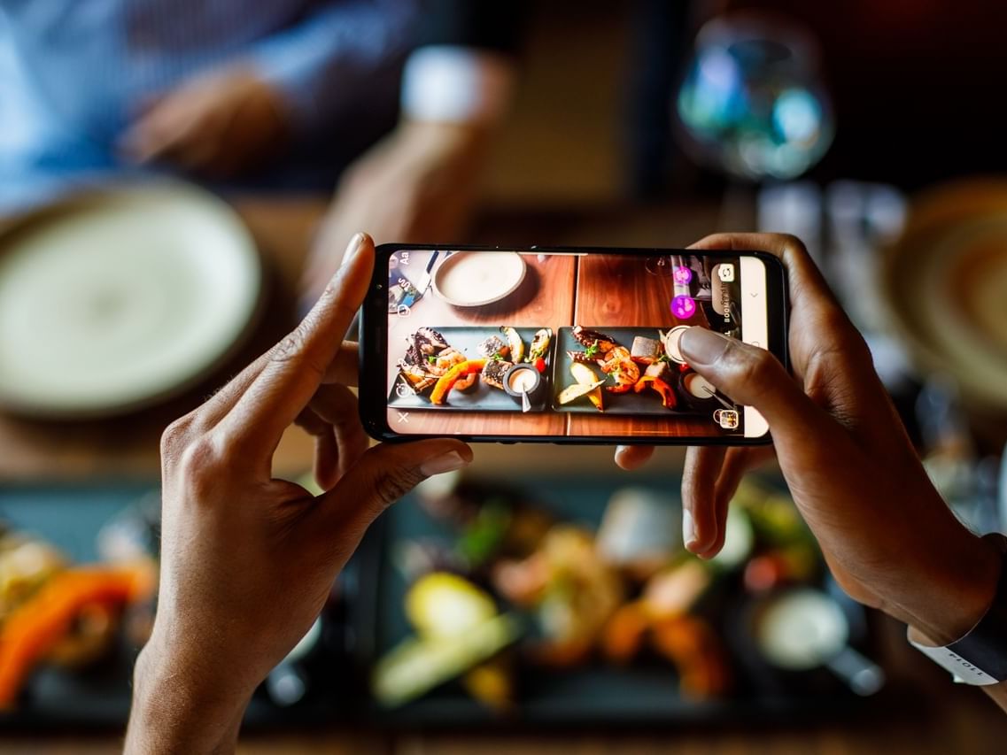 Guest taking a picture of served dishes in Pacific Groove Restaurant & Lounge at Paramount Hotel Dubai