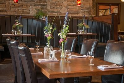 Leather chairs, dining tables with a stone wall behind the partition at Fork Seasons, Hilltop Inn Salmon Arm