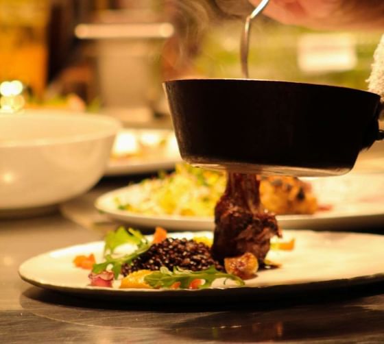 A person serving food onto a dish from a pan in a restaurant kitchen at The Clifton