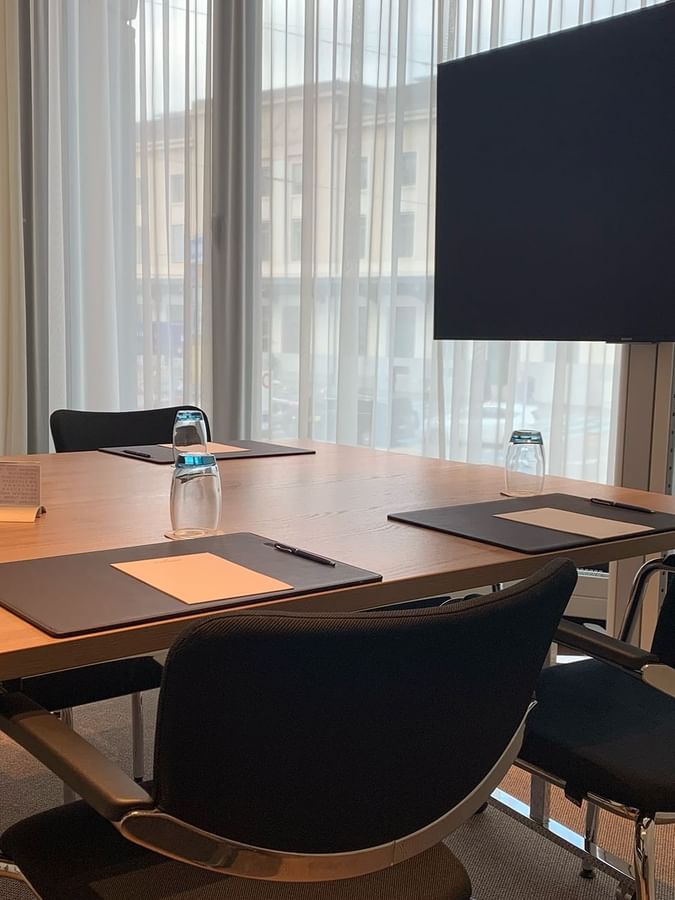 Flat screen monitor by a wooden table and black chairs in Cornavin at Warwick Geneva