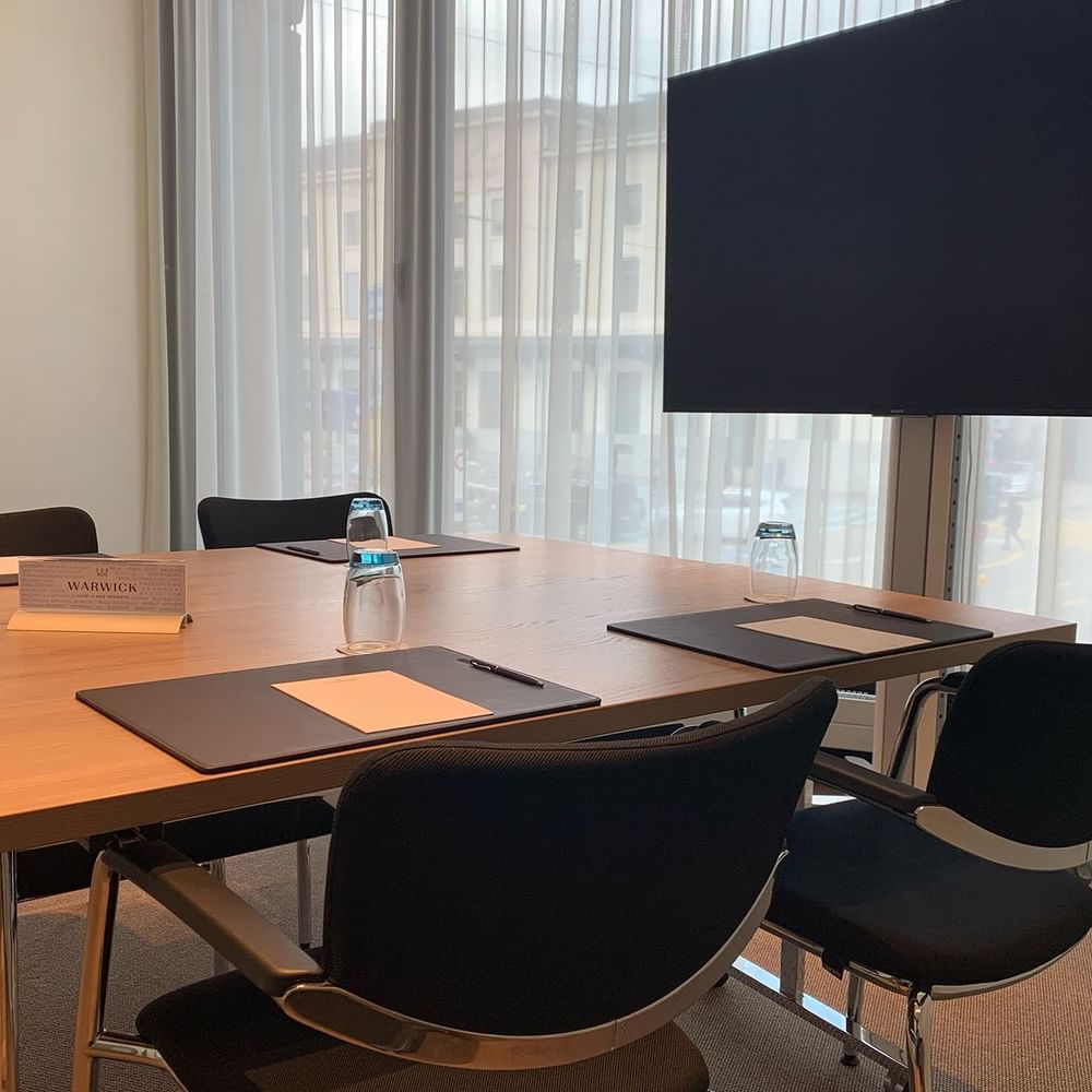 Flat screen monitor by a wooden table and black chairs in Cornavin at Warwick Geneva