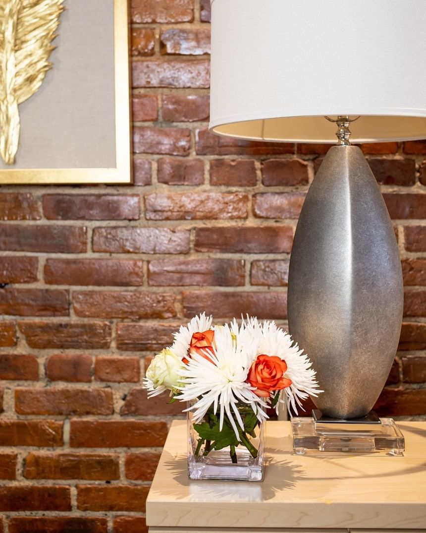 a bedside table with a lamp and a vase of flowers, exposed brick