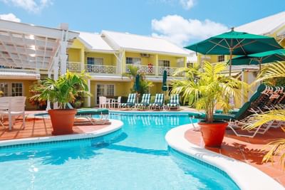 Hotel courtyard featuring a sparkling pool surrounded by green plants, loungers, and yellow buildings at Bay Gardens Hotel