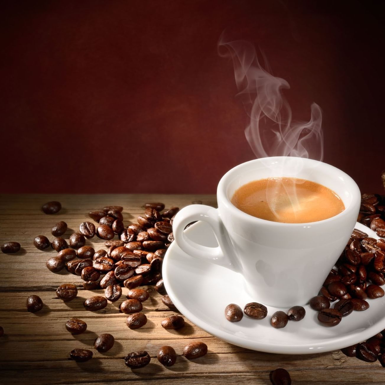 Taza de café humeante sobre un plato, rodeada de granos de café en una mesa de madera.