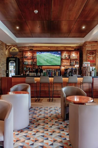 Zoe Bar at Habitel Hotel Select, with armchairs, bar stools, and a TV showing a soccer match, perfect for Bogota dining​