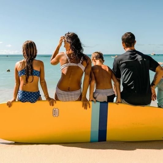 Family sitting on a surfboard by the beach near Waikiki Resort Hotel by Sono