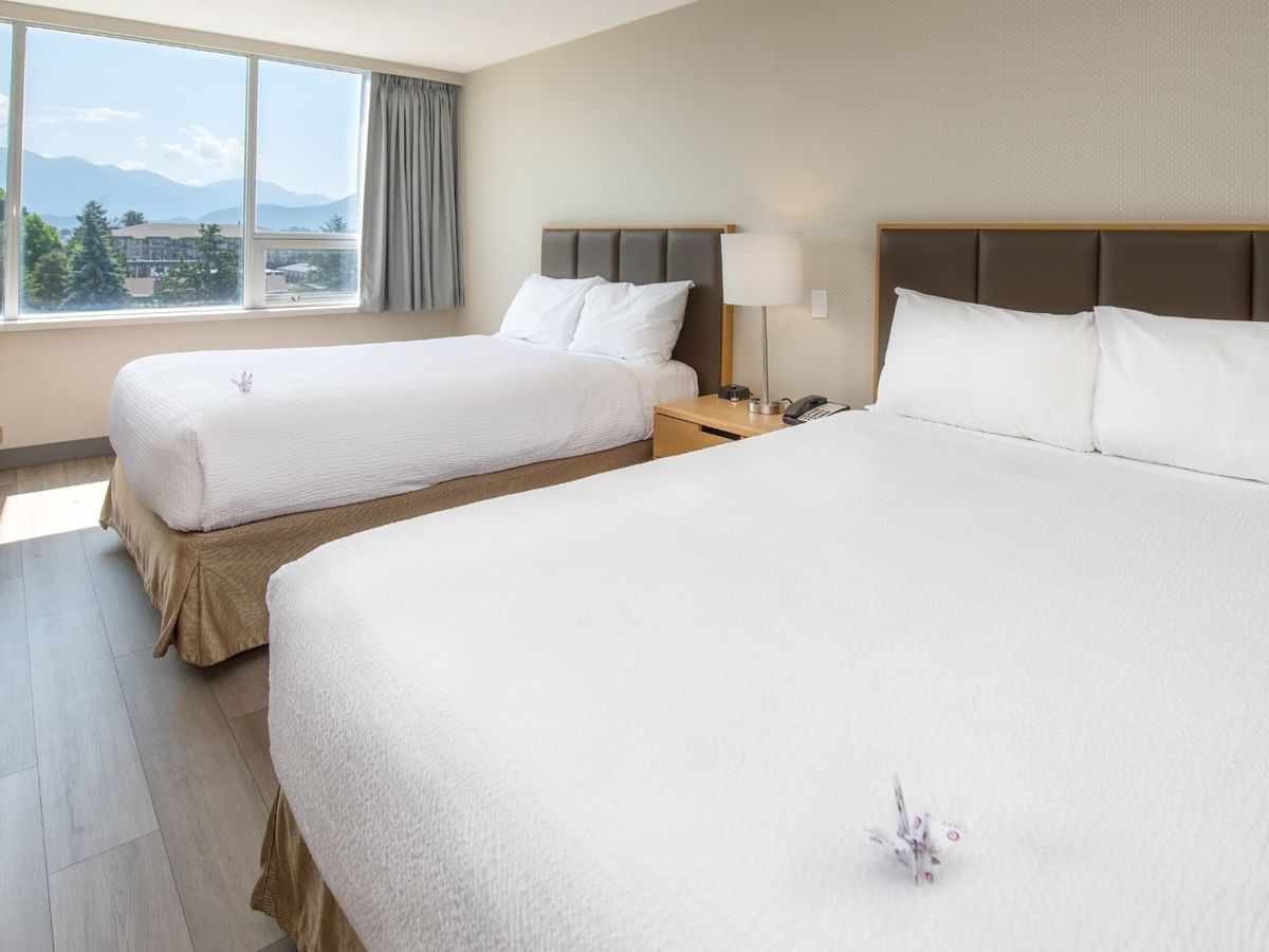 Two beds, a chair, a nightstand, and a large window showing mountains.