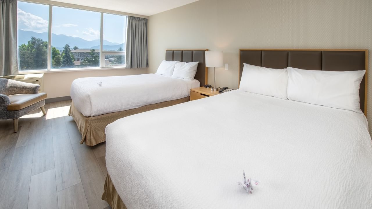 Two beds, a chair, a nightstand, and a large window showing mountains.