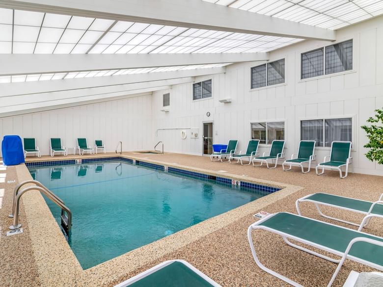 An indoor pool with blue water and green lounge chairs around it.