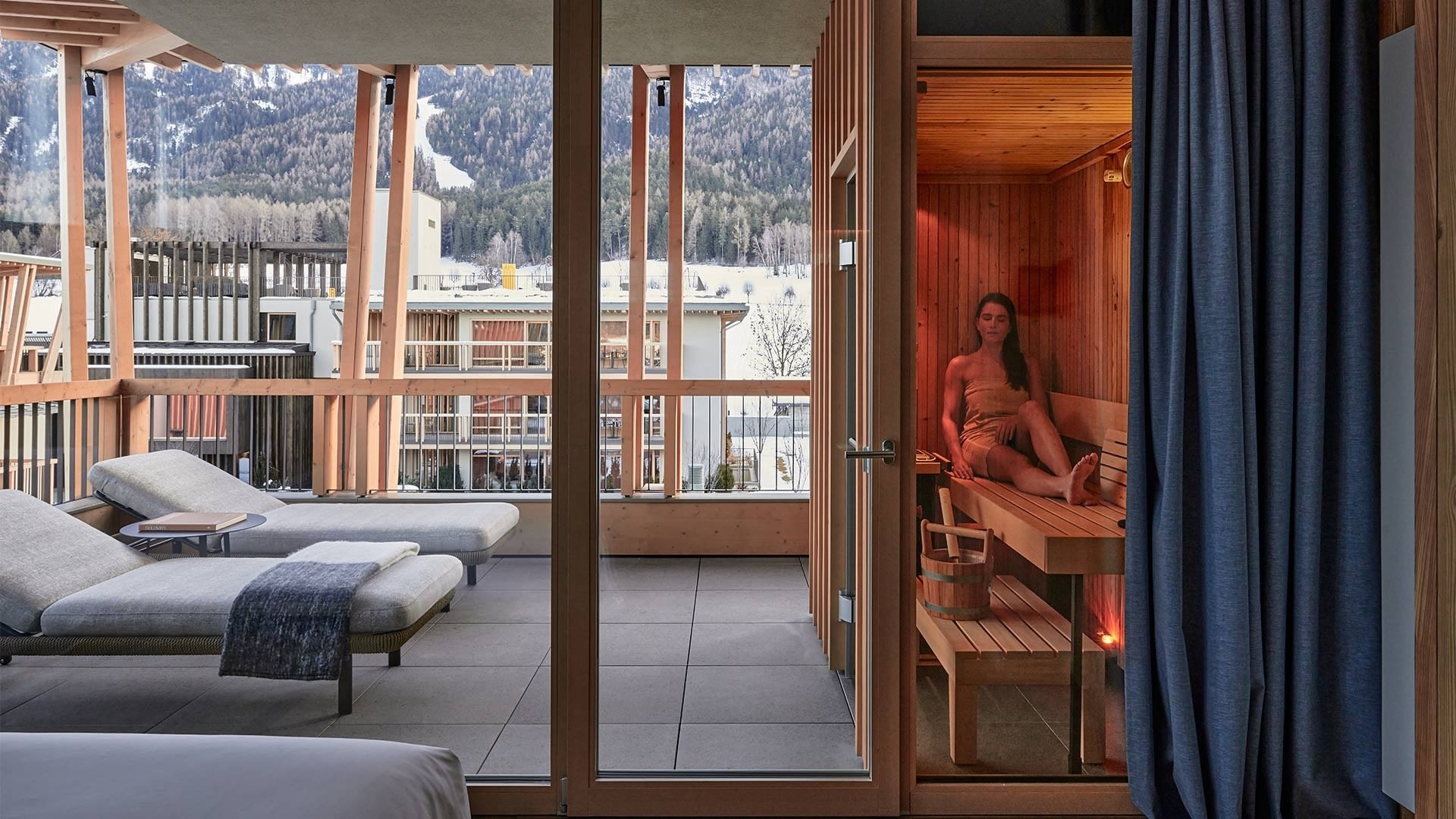 Saunabereich mit Frau auf Holzbank und Liegen draußen mit Bergblick.