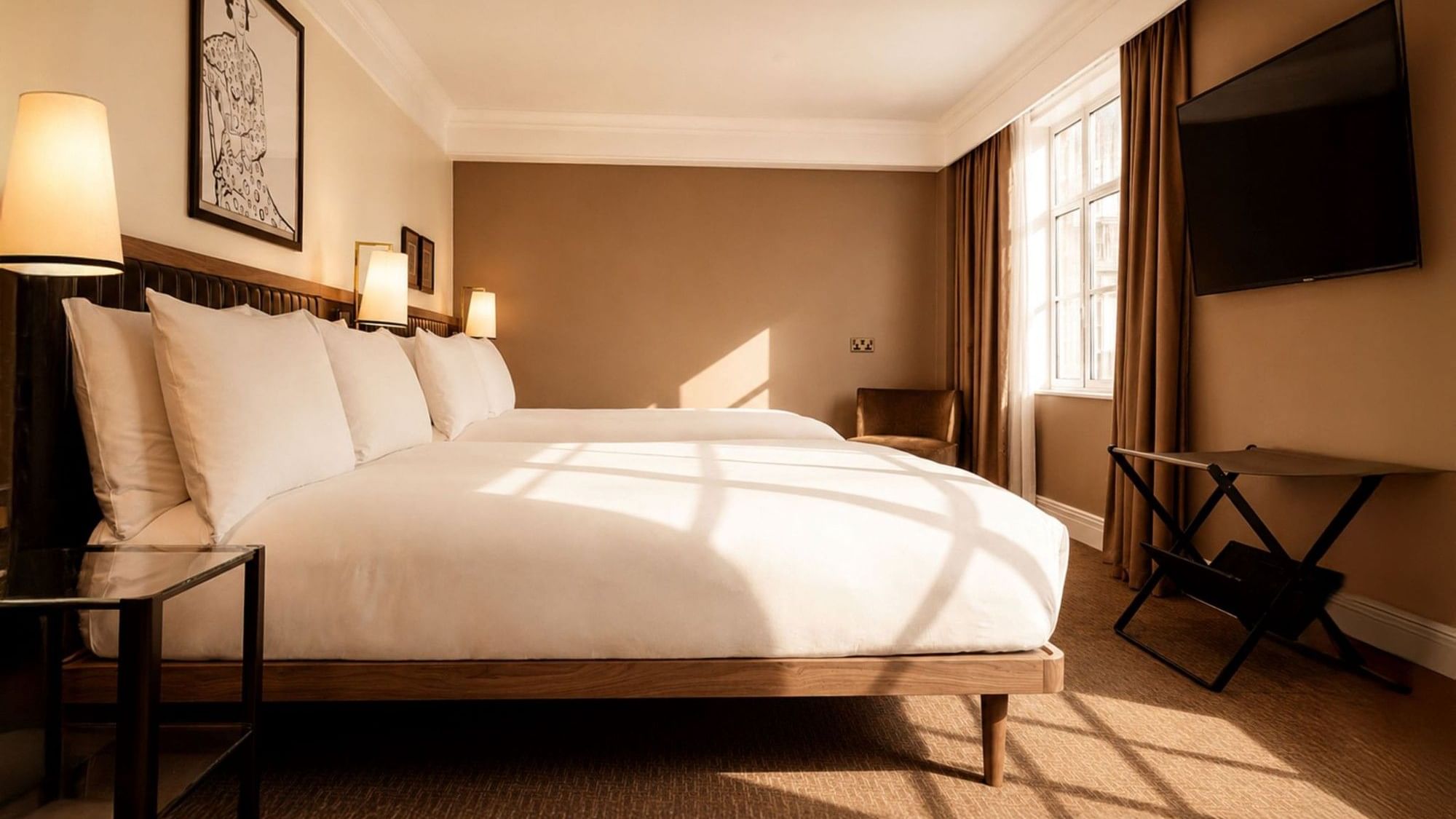Sunlit Family Room with white bedding, warm beige walls, flat-screen TV, and wooden accents at The May Fair Hotel, London.